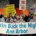 U-M students Catherine Herron, left, and Kathleen Carbone, center, and Detroit Mercy student Megan Gardner hold up a sign and march with others for the Take Back the Night rally in Ann Arbor. Angela J. Cesere | AnnArbor.com
